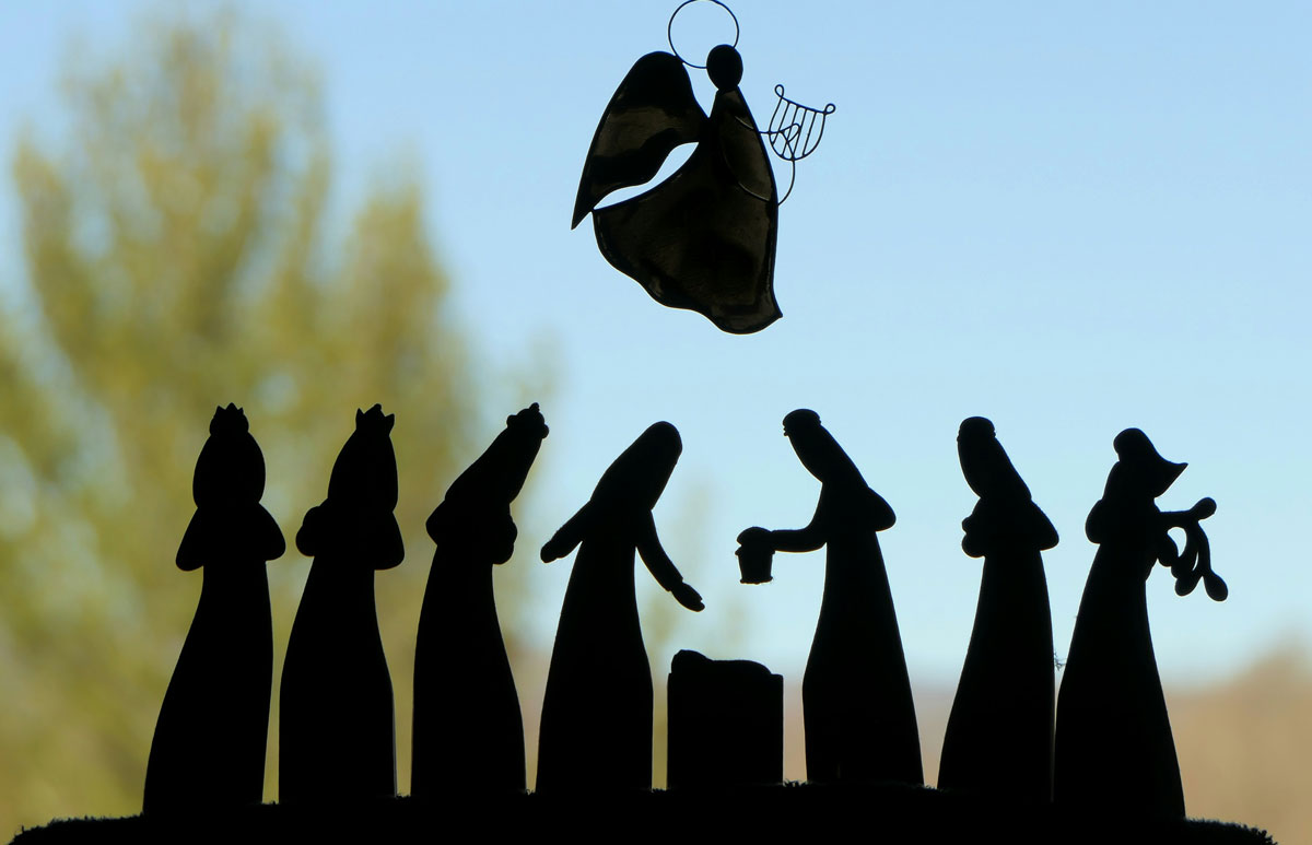 Nativity scene black silhouette against a blue sky with an angel in the air